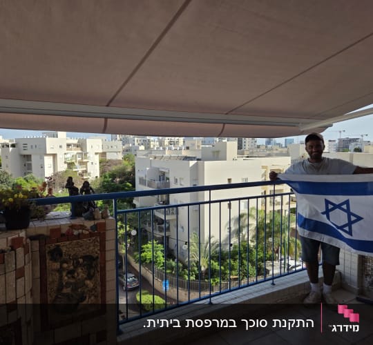 אדם מחזיק דגל ישראל במרפסת עם סוכך
